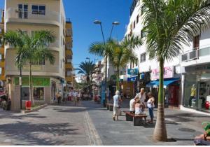 une rue avec des palmiers et des personnes marchant dans une rue dans l'établissement Apartamento en Los cristianos 2 habitaciones 4 huespedes Vv Elenita, à Los Cristianos