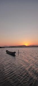 ein Boot, das bei Sonnenuntergang im Wasser sitzt in der Unterkunft Chalés com vista para Lagoa de Ibiraquera in Imbituba