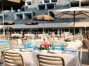 una mesa con mesas blancas, sillas y sombrillas en PFA Hotel La Darsena - Follonica, en Puntone di Scarlino