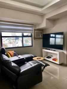 a living room with a black leather couch and two windows at Horizon 101 - champito's place in Cebu City