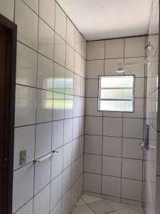 uma casa de banho em azulejos brancos com um chuveiro e uma janela em Pousada Ana e o Mar em Ubatuba