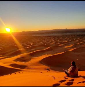 een persoon die in de woestijn zit te kijken naar de zonsondergang bij Chegaga Luxury Camp in El Gouera