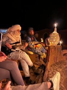 Chegaga Luxury Camp في El Gouera: مجموعة من الناس يجلسون حول طاولة في الليل
