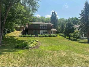 a large house on a grassy hill with trees at Lake Cabin; Renovated, Flat Lot, Dock, Sandy Beach, Many Games and Lake Toys! in Annandale