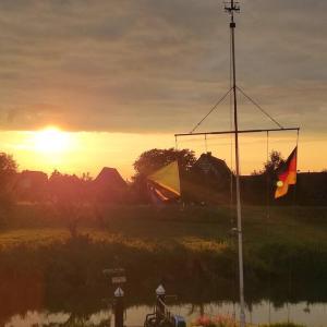 a sunset over a field with a river and a flag at Gästewohnung von J&O am Fluss. in Jork