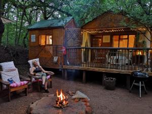 a woman sitting next to a fire in front of a cabin at Iris Retreat & Island Day Spa in Hartbeespoort