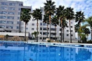 a large swimming pool with palm trees in front of a building at Fuengirola - Luxury 3 bedrooms apartment in Fuengirola