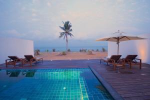 a swimming pool with chairs and an umbrella and the beach at Jetwing Thalahena Villas in Negombo