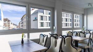eine Reihe von Tischen und Stühlen in einem Zimmer mit Fenstern in der Unterkunft Hotel 83 in Bonn