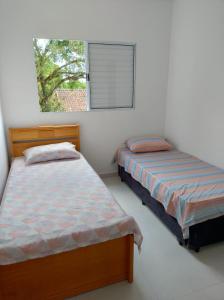 two beds in a white room with a window at Casa da Praia: o mar a apenas 500 metros de você in Itanhaém