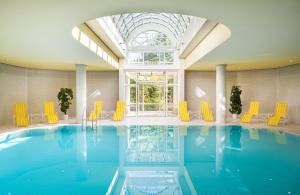 une piscine avec des chaises jaunes et une grande fenêtre dans l'établissement Leonardo Hotel Weimar, à Weimar