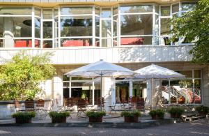 two tables with umbrellas in front of a building at Leonardo Hotel Weimar in Weimar