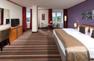 ワイマールにあるレオナルド ホテル ワイマールの大型ベッド1台、薄型テレビが備わるホテルルームです。