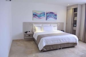 een slaapkamer met een groot wit bed en 2 schilderijen aan de muur bij Radisson Diamond Barranquilla in Barranquilla