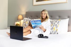 una mujer sentada en una cama leyendo un libro en Quest Cronulla Beach, en Cronulla