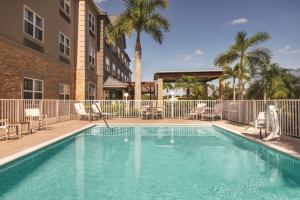 una piscina con sillas, un edificio y palmeras en Country Inn & Suites by Radisson, Bradenton-Lakewood-Ranch, FL, en Bradenton