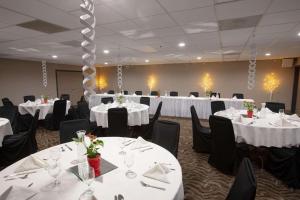 Country Inn & Suites by Radisson, Fargo, ND في فارغو: قاعة احتفالات بالطاولات البيضاء والكراسي السوداء