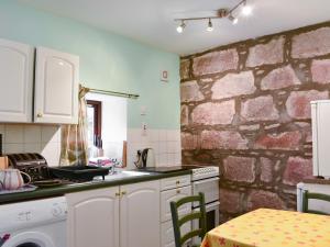 a kitchen with white cabinets and a brick wall at Pine Tree Cottage - Uk45925 in Ballater
