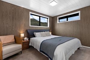 a bedroom with a bed and a chair and two windows at The Headley Loft in Queenstown