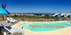 a swimming pool with chairs and an umbrella and the ocean at Unique Hotel & Suites in Punta Del Diablo