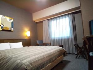 a hotel room with a bed and a window at Hotel Route-Inn Ashikaga Ekimae in Ashikaga