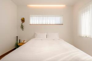 a white bed in a white bedroom with a window at Tov & Kara in Jeju
