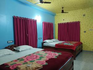 duas camas num quarto com cortinas vermelhas e lençóis vermelhos em SURYA VILLA GUEST HOUSE em Tajpur