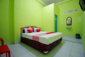 a bedroom with a bed with green walls and red pillows at OYO 2585 Sherren Guest House in Lubuklinggau
