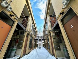 una vista de un callejón entre dos edificios en la nieve en 1-3サン　地下鉄徒歩圏内サービスアパ―トメントSAPPORO Shiroish iStation エアコンネット完備 en Tsukisappu