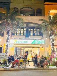 a group of people sitting at tables in front of a building at Novaworld Phan Thiết- 7Days mart in Phan Thiet