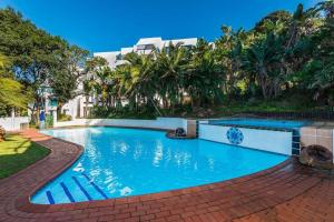 a swimming pool in a resort with trees and a building at Santorini Beach Views - 23 Perissa in Ballito