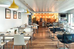 a restaurant with white tables and chairs and a kitchen at Zenitude Hôtel Résidences Roissy Village in Roissy-en-France