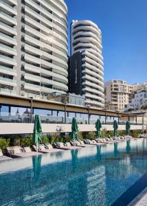 a pool with chairs and umbrellas in front of buildings at Barceló Fortina Malta in Sliema