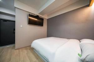 1 dormitorio con 1 cama blanca y TV en la pared en Lime Hotel, en Busan
