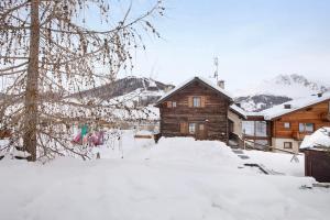 uma cabana de madeira na neve em frente a uma casa em Appartamento Gemma em Livigno