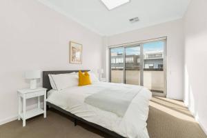 a white bedroom with a large bed with a yellow pillow at Spacious 3 bed apartment near airport with parking in Sydney