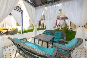 a patio with blue chairs and a table and white curtains at Poykent Naqshband in Bukhara