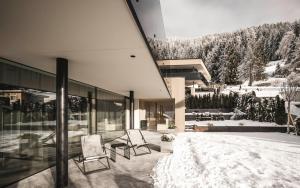 a house with two chairs on a patio in the snow at Timeless Dolomites Apartments in Dobbiaco