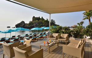a patio with chairs and tables and a view of the ocean at La Plage Resort in Taormina