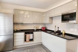 cocina con armarios blancos y nevera de acero inoxidable en Paradigm House, Delightful 2-Bedroom Flat 4, Oxford en Oxford
