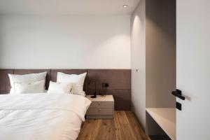 a bedroom with a bed with white sheets and pillows at Timeless Dolomites Apartments in Dobbiaco