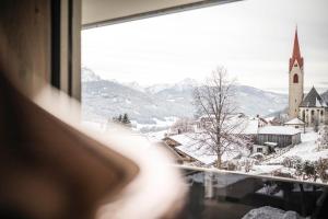 a window with a view of a church in the snow at Timeless Dolomites Apartments in Dobbiaco