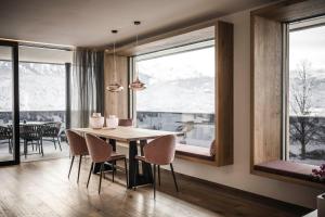 a dining room with a table and chairs and windows at Timeless Dolomites Apartments in Dobbiaco