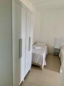 a white bedroom with a bed and a cabinet at MDJ Suítes in Cabo Frio