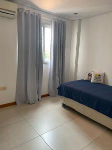um quarto com uma cama com lençóis azuis e uma janela em Zona shopping del Sol, Asunción em Assunção