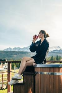 Eine Frau, die auf einem Fass sitzt und ein Glas Wein trinkt. in der Unterkunft Góralski Harem Osada Glamp Jacuzzi & Balia in Zakopane