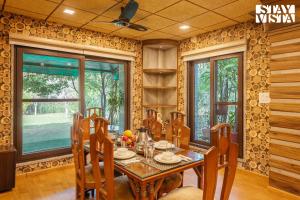 a dining room with a table and chairs and windows at StayVista's Apple Farms - Urban Oasis with Outdoor Pool & Expansive Lawn in Sohna
