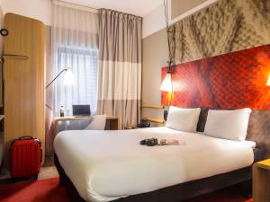 una camera d'albergo con un grande letto e una valigia rossa di ibis Paris Place d’Italie 13ème a Parigi