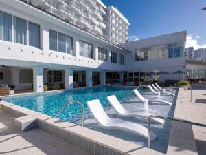 Hilton Garden Inn San Juan Condado في سان خوان: مسبح وكراسي بيضاء في مبنى