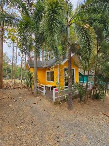 una casa amarilla con palmeras delante en Baan Rai Somkiat Homestay Saraburi, en Ban Lam Thong Lang